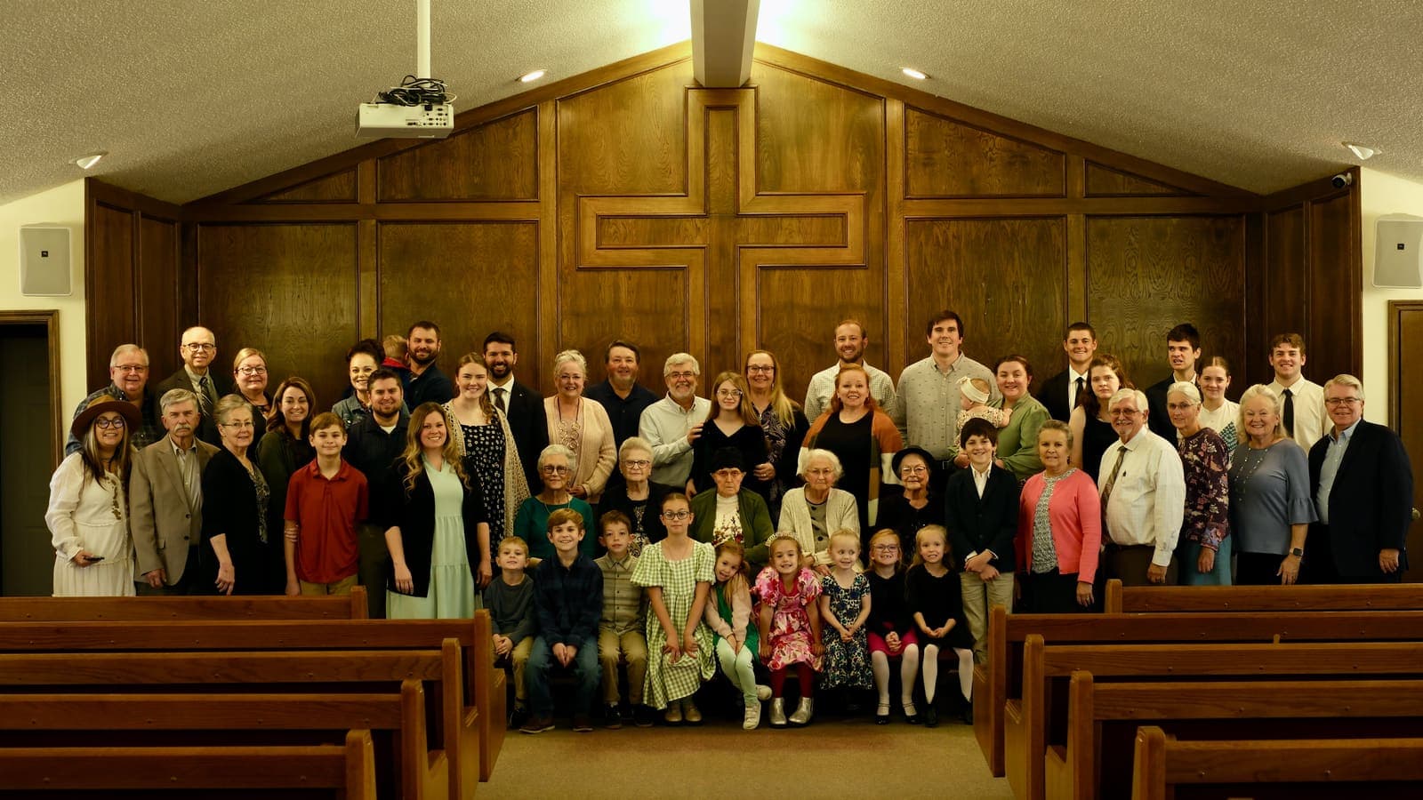 The Harrisonville Church of Christ congregation, several generations together at the front of the auditorium beneath the wooden cross