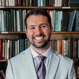 Isaac Moreno smiling in a light gray suit in front of a wall of books