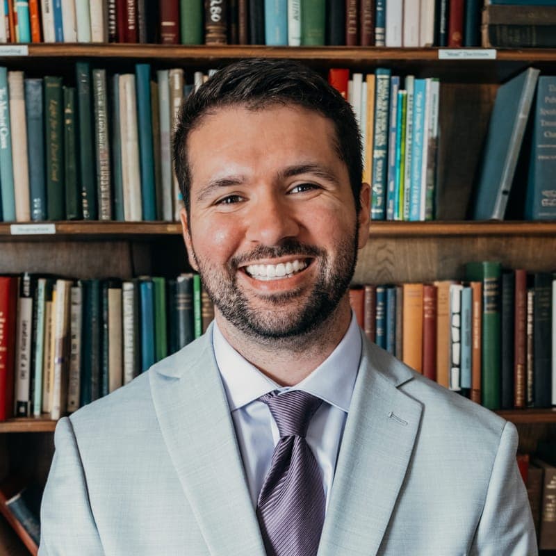 Isaac Moreno smiling in a light gray suit in front of a wall of books