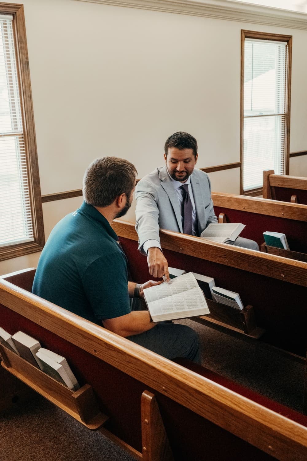 An older and a younger member of the congregation lean over an open book together across the pews