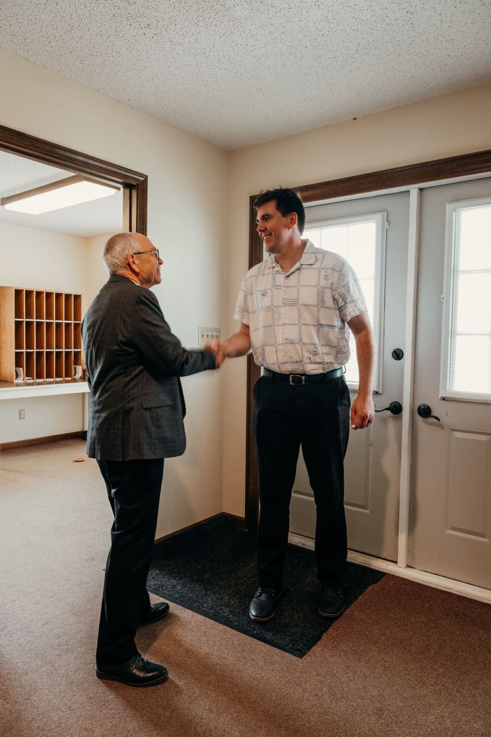 A member welcomes a visitor with a handshake just inside the front door of the building